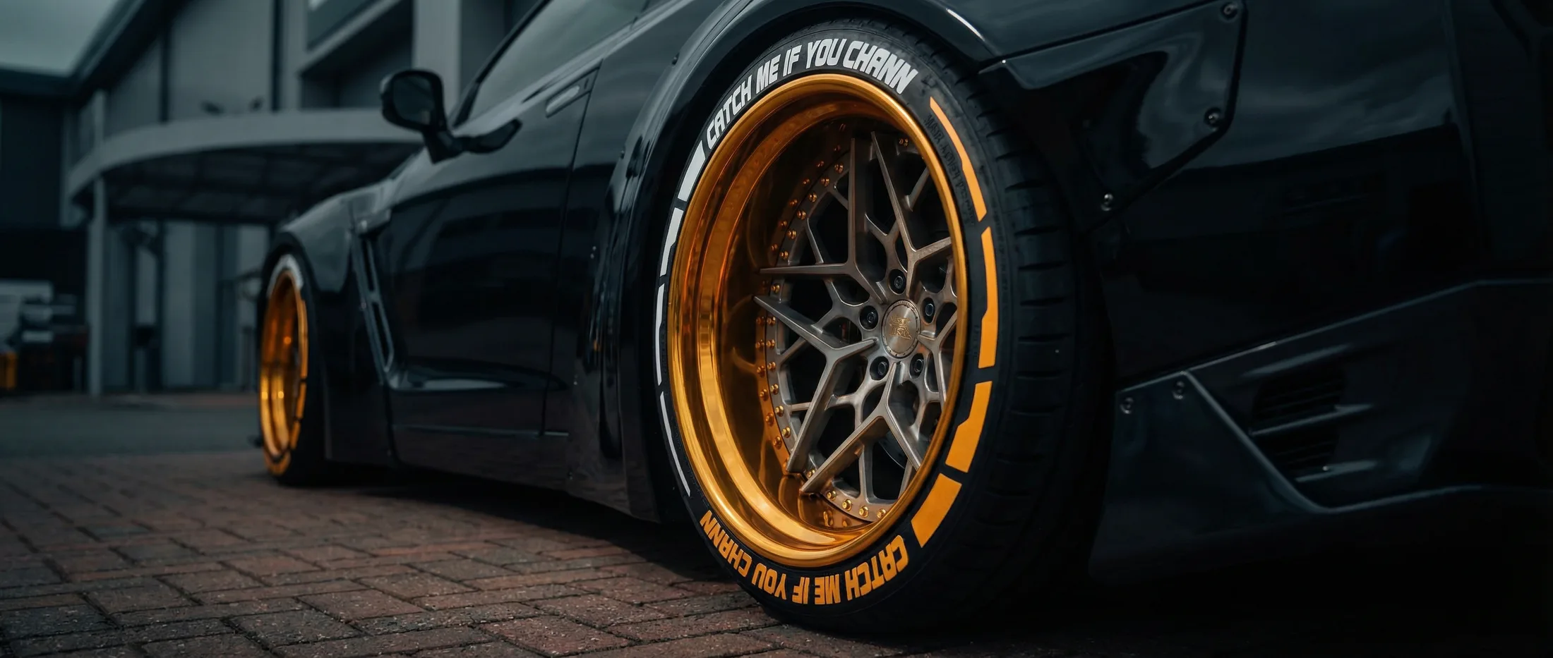 A black sports car on gold split-rim wheels, with permanent white and gold lettering around both tyre sidewalls.